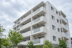 曇り空の下の、ごく普通の中規模の白いマンションの外観を少し見上げる角度で写した写真